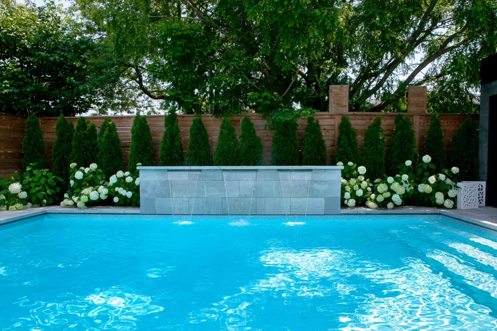 Modern Toronto backyard with an inground salt water pool, stone waterfall feature, cedar fencing, evergreens, and hydrangeas creating a private resort-style outdoor space.