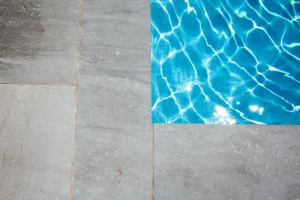 Close view of grey stone pool coping meeting the water at the pool edge