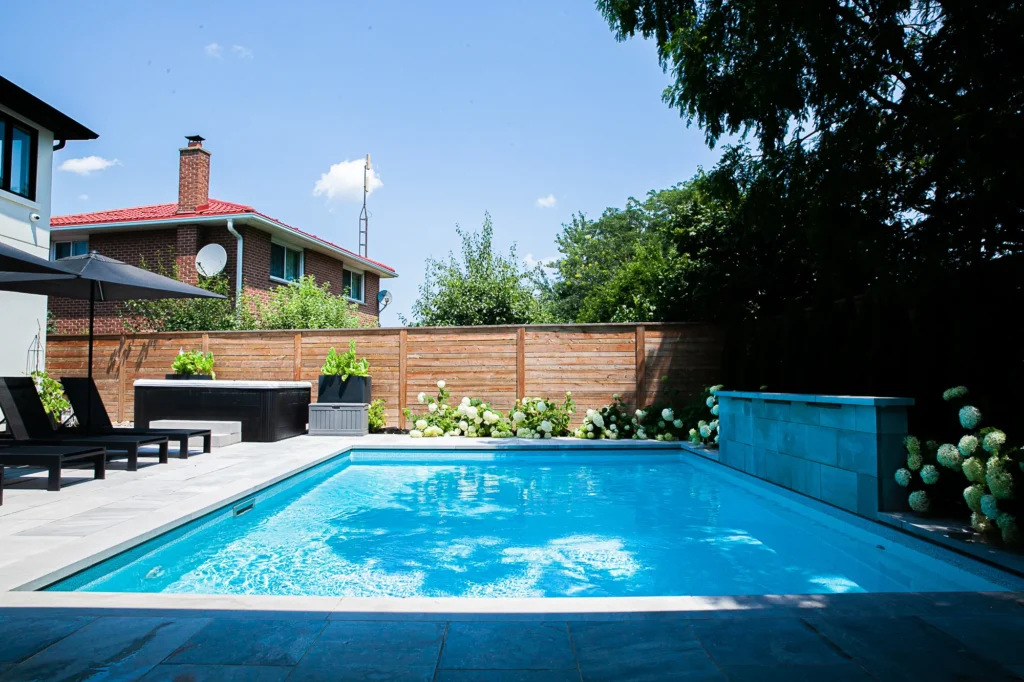 Modern Toronto backyard with an inground salt water pool, stone waterfall feature, cedar fencing, evergreens, and hydrangeas creating a private resort-style outdoor space. With retaining wall. Hardscaping elements too like interlock and plants