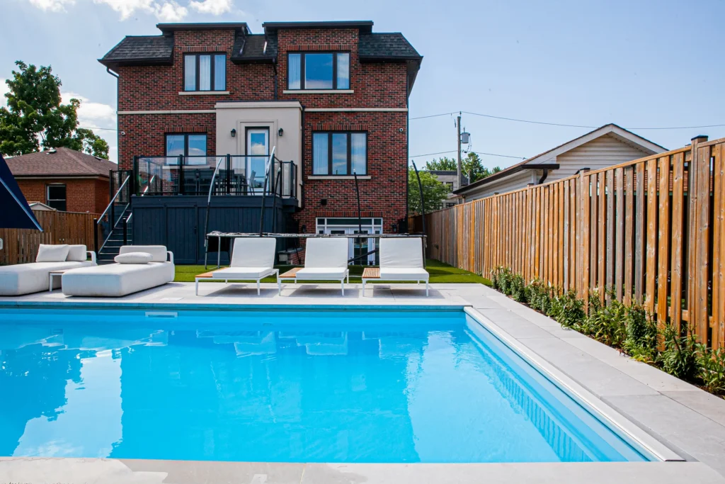 Small backyard pool in Toronto with a deck, lawn chairs by Destination Pools and Landscaping