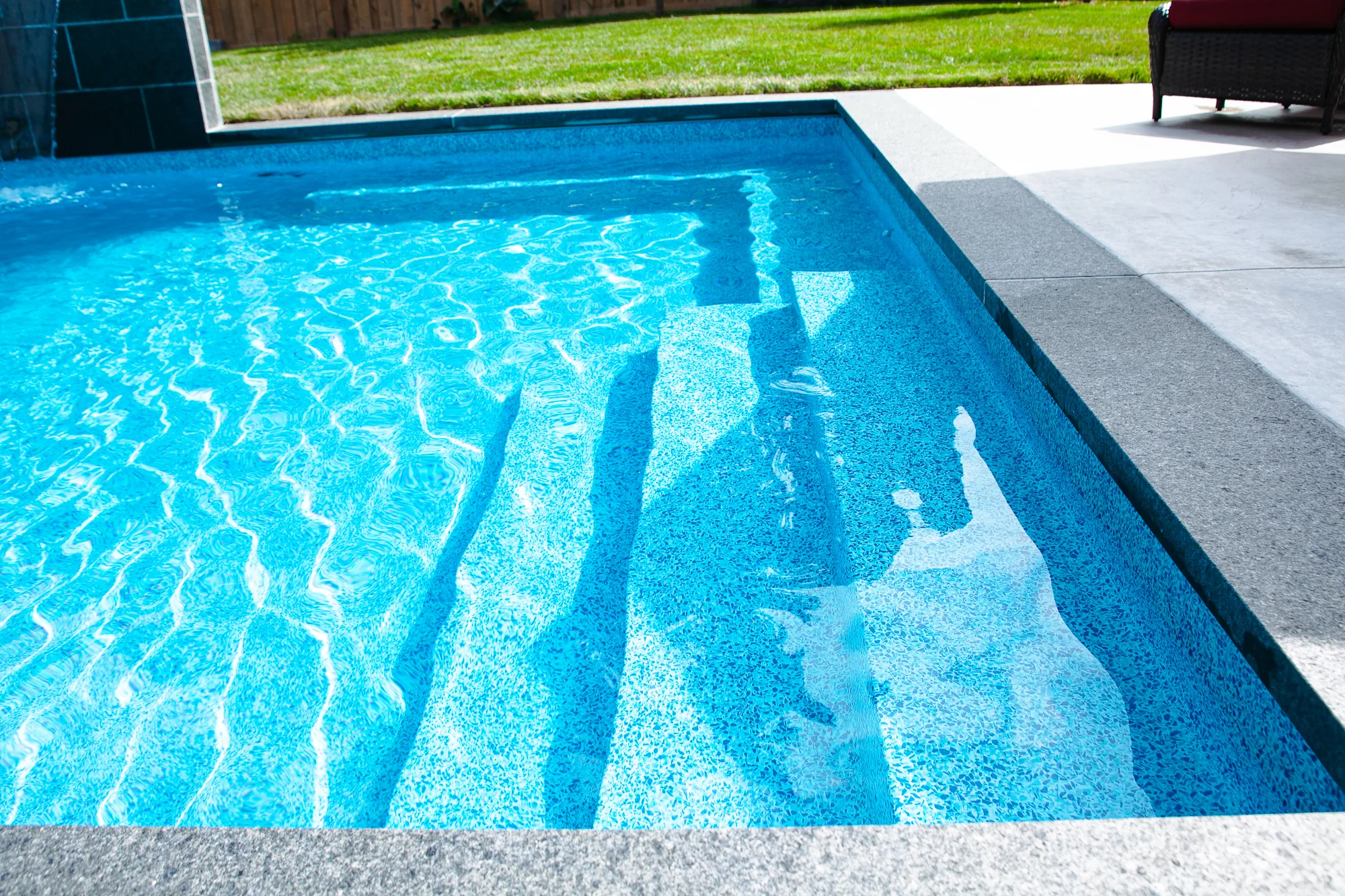 Close-up of the shallow end of a rectangular inground pool showing blue pebble aggregate vinyl liner, entry steps, and grey coping - Mississauga pool by Destination Pools and Landscaping