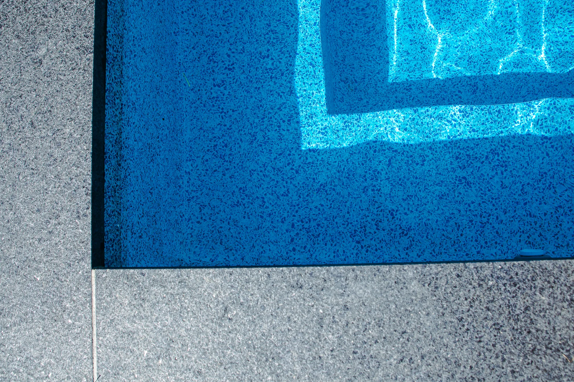 Detail close-up of the inground pool corner showing blue pebble aggregate vinyl liner and dark grey coping edge - Mississauga pool installation by Destination Pools and Landscaping